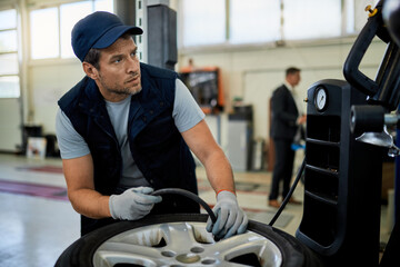 Auto repairman checking pressure in car tire in a workshop.