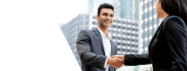 Smiling handsome young Indian businessman making handshake with businesswoman in the city, panoramic web banner with copy space