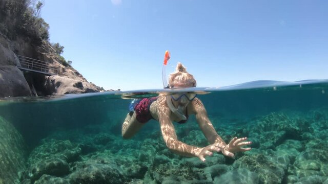 Woman snorkeler in Saint Andrew beach with reef and fishes of Elba island. Woman underwater snorkeling in Tyrrhenian sea on holiday travel, Italy. Saint andrew is Tuscan archipelago NP marine reserve.
