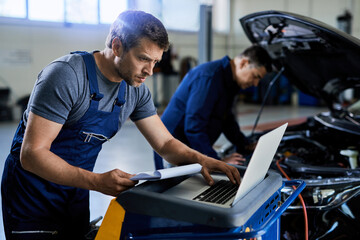 Auto repairman using laptop while working with a colleague in a workshop.