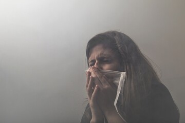 Young Hispanic female with scrunched eyes in horror holding a mask to her face covered in fog