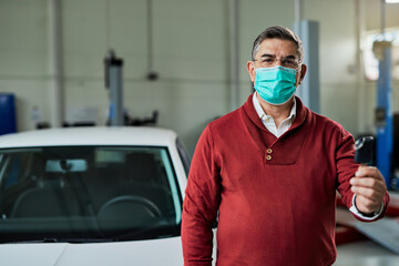 Fototapeta na wymiar Mid adult man wearing protective face mask while holding car key in auto repair shop.