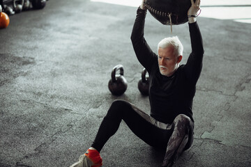 Obraz na płótnie Canvas Senior man exercising at gym. Mature man exercising with medicine ball.