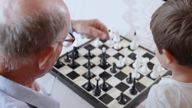 chess, a happy intelligent male child plays with his loving elderly grandfather in board educational games sitting at a table in the room