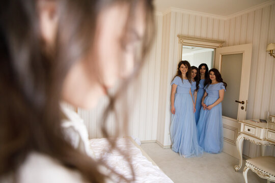 happy bridesmaids standing and watching at the beautiful bride