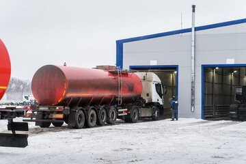 Oil tanker truck with a red tank drives into a box at a service station