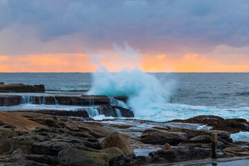 Wave strikes rock formation on the coastline.