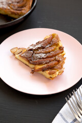 Homemade Apple Dutch Pannekoek Pancake on a pink plate on a black background, side view.