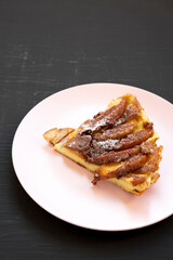 Homemade Apple Dutch Pannekoek Pancake on a pink plate on a black background, low angle view. Copy space.