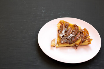 Homemade Apple Dutch Pannekoek Pancake on a pink plate on a black surface, low angle view. Copy space.