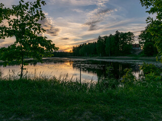 image with a beautiful colorful sunset over the lake, in the foreground the contours of trees and grass, Lielais Ansis, Rubene, Latvia