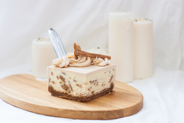 Slice of caramel cheesecake with whipped cream, cookies, gingerbread and cinnamon on white background.