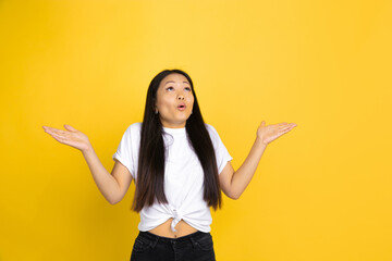 Showing. Portrait of young asian woman isolated on yellow studio background. Stylish, trendy. Beautiful brunette model. Human emotions, facial expression, sales, ad, shopping concept. Copyspace.