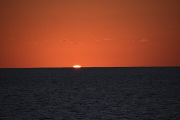 Sunset on the Atlantic Ocean. Unusual color of orange and red during light refraction. Sea has black color and picture is made from merchant cargo container vessel.