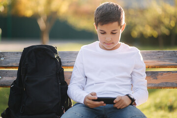 Teenage boy play online games on his smartphone in the park after lessons in school