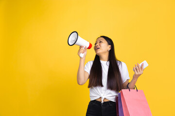 Shouting. Young asian woman with colorful shopping packages on yellow studio background. Stylish, trendy. Beautiful brunette. Human emotions, facial expression, sales, ad, shopping concept.