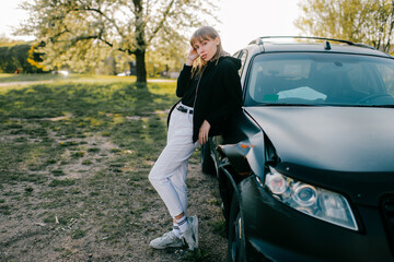 Beautiful young caucasian woman in white jeans, white trainers and black jacket take photos with black broken car