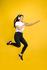 Fototapeta na wymiar Jumping high, happy with headphones. Young asian woman portrait on yellow studio background. Stylish, trendy. Beautiful brunette. Human emotions, facial expression, sales, ad, shopping concept.