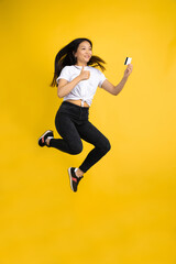 Fototapeta na wymiar Online purchase. Jumping high, happy. Young asian woman portrait on yellow studio background. Stylish, trendy. Beautiful brunette. Human emotions, facial expression, sales, ad, shopping concept.
