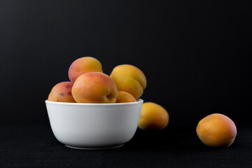 Bowl with ripe apricots on a black background