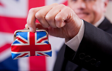 Stereotypical English businessman holding a Union Jack money purse. The man is wearing a dark business suit and bowler hat, with a Union Jack flag background.