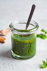 Fresh traditional chimichurri sauce for barbecue meat in glass jar, light background.