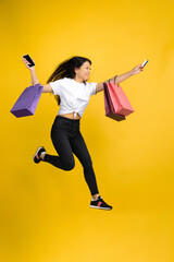 Fototapeta na wymiar Jumping high, happy. Young asian woman with colorful shopping packages on yellow studio background. Stylish, trendy. Beautiful brunette. Human emotions, facial expression, sales, ad, shopping concept.