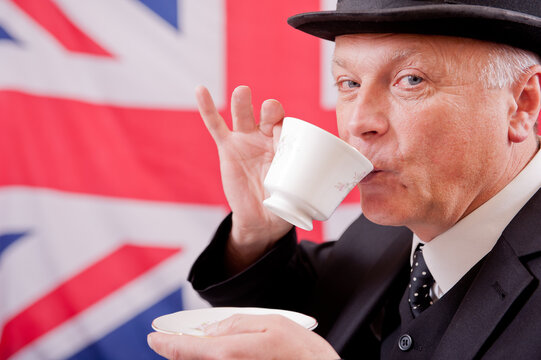 Englishman drink tea, wearing a dark suit with a bowler hat, with a Union Jack flag background.