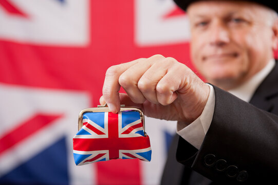 Stereotypical English businessman holding a Union Jack money purse. The man is wearing a dark business suit and bowler hat, with a Union Jack flag background.