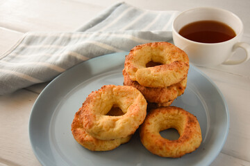 Appetizing baked bagels on a blue plate on a white wooden background with a white mug of tea and a kitchen towel