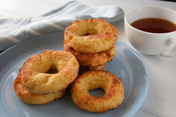 Appetizing baked bagels on a blue plate on a white wooden background with a white mug of tea and a kitchen towel