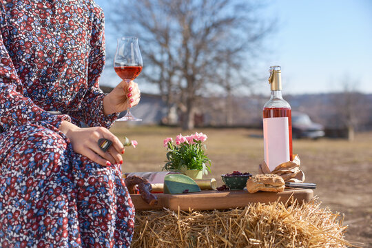 Outdoors table with plate of appetizers and bottle with blank etiquette for mockup. girl with a glass of wine in her hands on a sunny day.