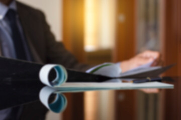 Blurred image of businessman sitting at the office desk and checking or proof the business data document file with checkbook on the desk at modern office with reflection. Business plan  concept