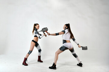 Plakat beautiful girls in costumes of robots quarreled and fight with a battle ax and a war hammer
