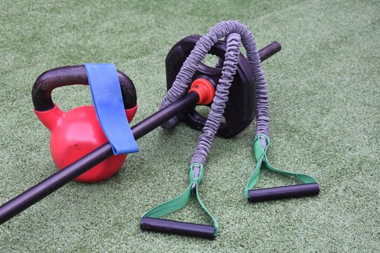 Closeup Of A Round Heavy Weight, Stretchy Gym Equipment, A Resistance Band And Lifting Bar On Grass