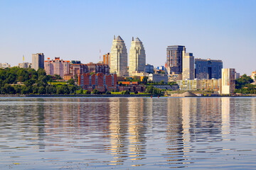 Big city on the banks wide river. Beautiful modern towers, buildings, skyscrapers are reflected in the water on summer morning. Ukrainian city Dnepropetrovsk, Dnipro, Ukraine