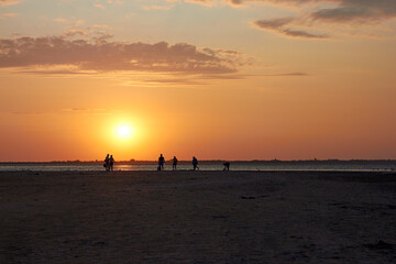 Fototapeta na wymiar Silhouettes of people walking at sunset near the lake
