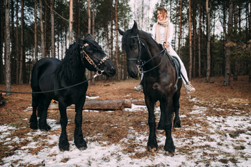 Fototapeta premium Elegant woman in a grey coat riding on a black horse