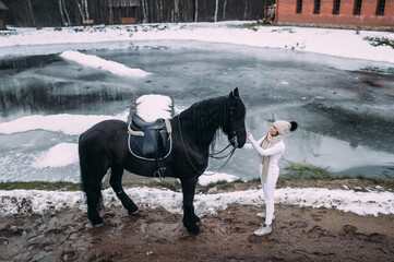Handsome young female in white trousers with a big black horse outside