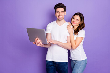 Portrait of positive couple man woman hold laptop work from home have online partnership communication wear white t-shirt casual style denim jeans isolated over violet color background