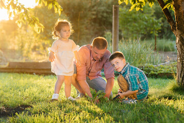 Little brother and sister are planting seedlings with their father in a beautiful spring garden at sunset. New life. Save the environment. Careful attitude to the surrounding world and nature