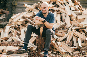 Picture of beautiful caucasian man stands with an axe against the background of a large pile of firewood