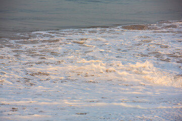 natural copy space shot of a wave crushing on the smooth yellow sand beach surface, forming white foam, with the blue sky on the horizon. Early morning sunrise at Pitiwella beach, Sri Lanka
