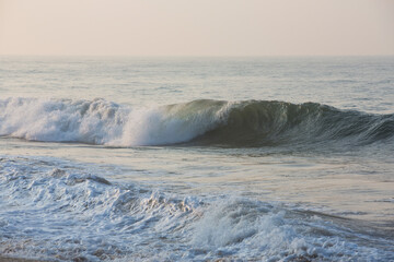 Obraz premium natural copy space shot of a wave crushing on the smooth yellow sand beach surface, forming white foam, with the blue sky on the horizon. Early morning sunrise at Pitiwella beach, Sri Lanka