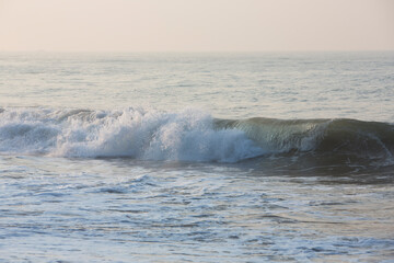 natural copy space shot of a wave crushing on the smooth yellow sand beach surface, forming white foam, with the blue sky on the horizon. Early morning sunrise at Pitiwella beach, Sri Lanka