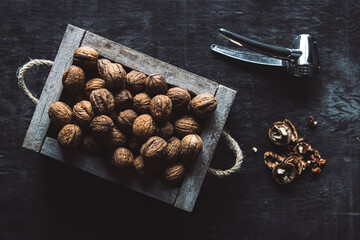 Box with tasty walnuts and nutcracker on dark wooden table, closeup