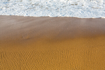 beautiful filled frame close up seascape wallpaper background shot of golden orange sand with white foamy waves of the Indian ocean forming pretty textures and patterns. Pitiwella beach, Sri Lanka