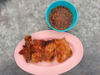 Grilled chicken on a pink plate Cut into pieces, chicken's skin has burn marks and chilli sauce.