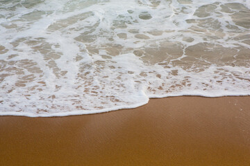beautiful filled frame close up seascape wallpaper background shot of golden orange sand with white foamy waves of the Indian ocean forming pretty textures and patterns. Pitiwella beach, Sri Lanka