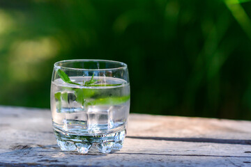Glass of water and mint. Close up of cocktail with  ice and mint leaves. Wooden table with natural green background.
